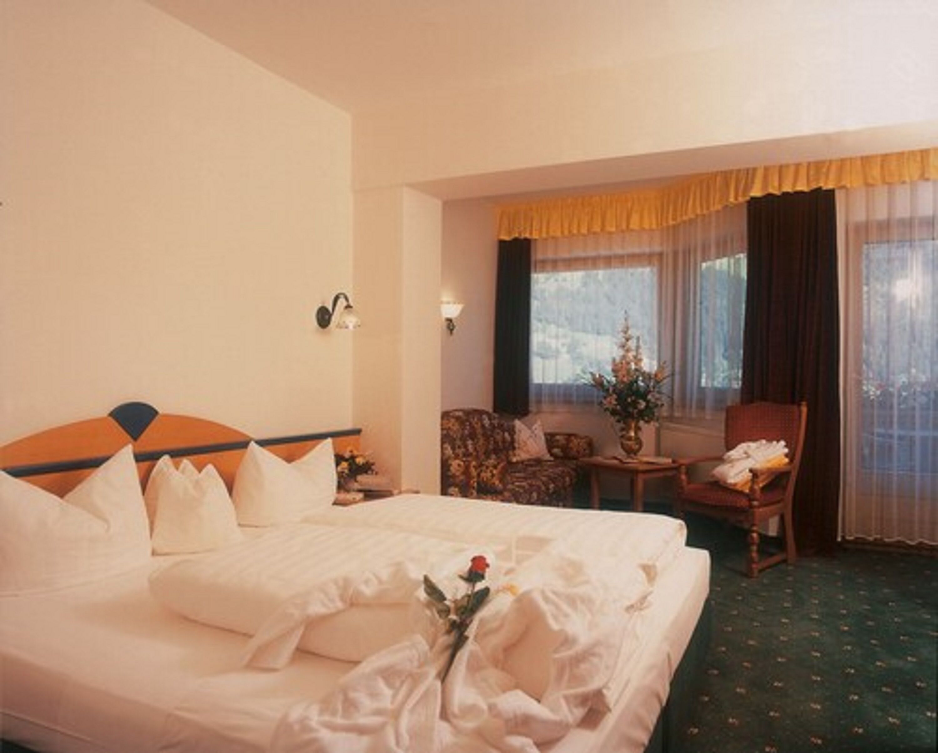 A hotel room with a large bed, a sitting area with a chair and a small table, and a window with curtains.