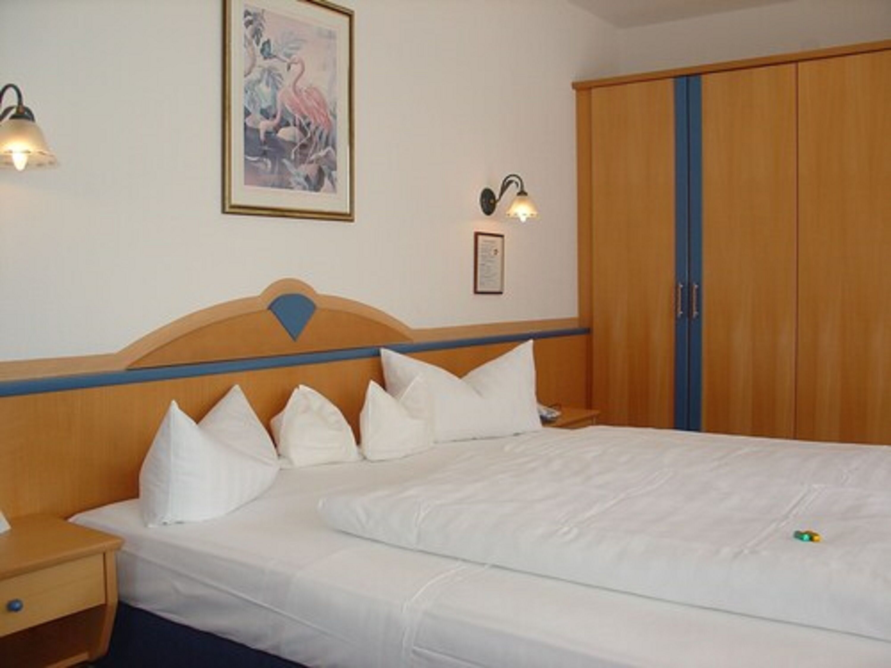 A hotel room with a bed, a nightstand, a wardrobe, and wall-mounted lighting.