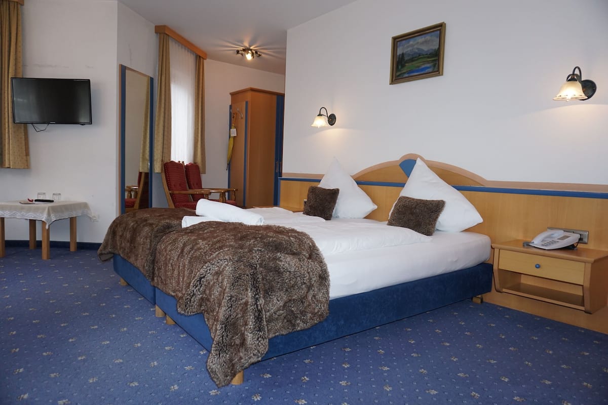 Habitación de hotel con una cama grande, una mesita de noche, una silla, un televisor y un cuadro en la pared.