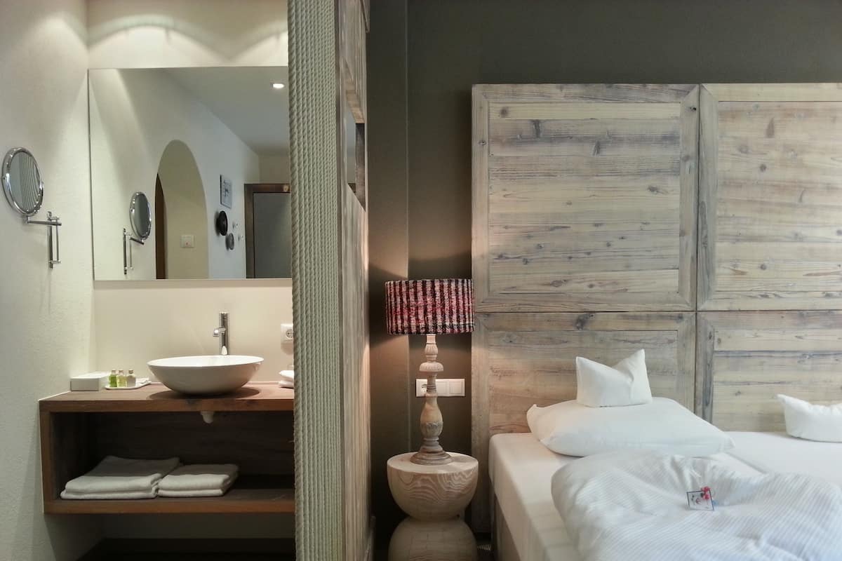 Habitación de hotel con tocador de madera, un espejo grande, una cama con ropa blanca y cabecera de madera.