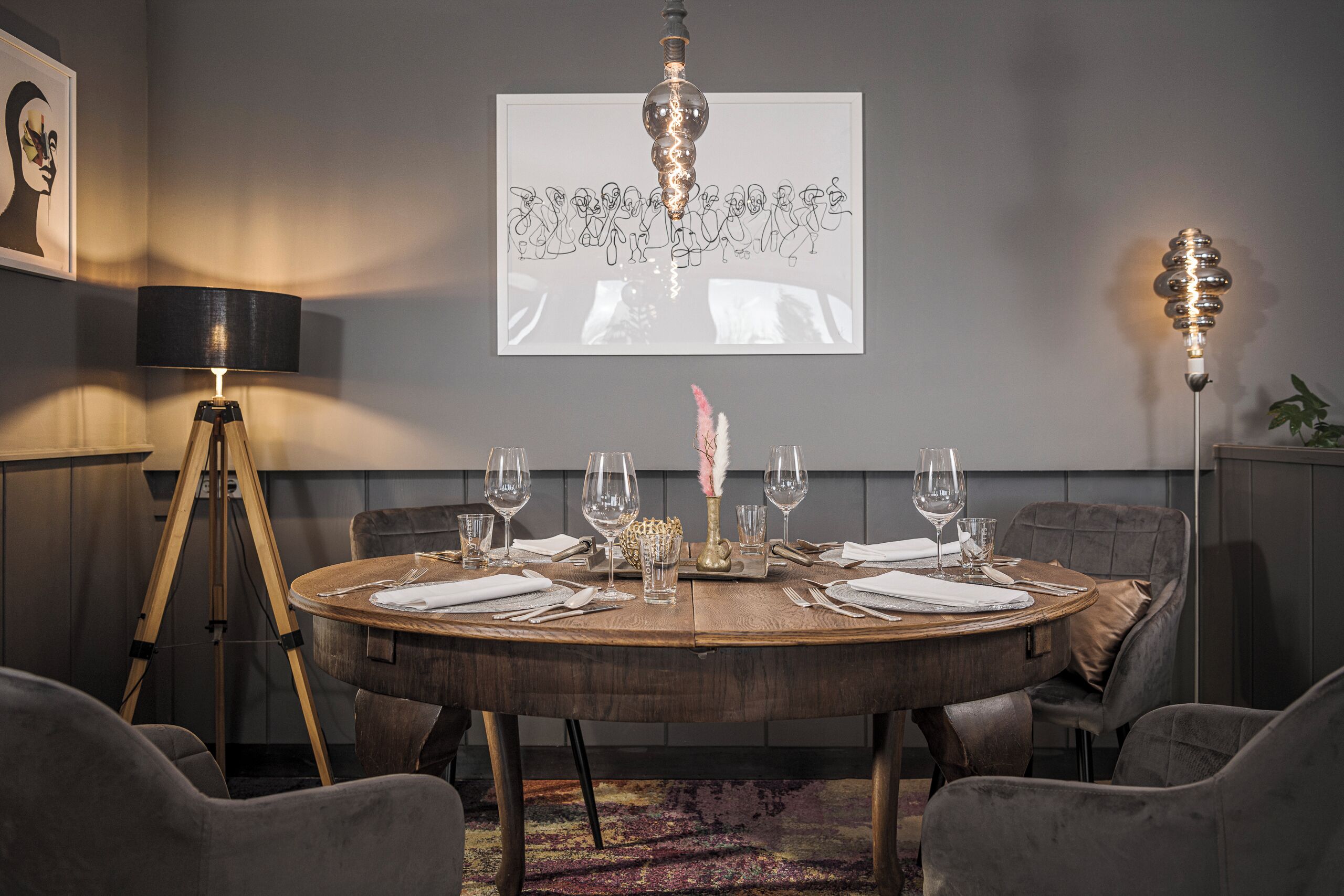 Een ronde eettafel gedekt met wijnglazen, een kaars en een beamer die een lijntekening projecteert.