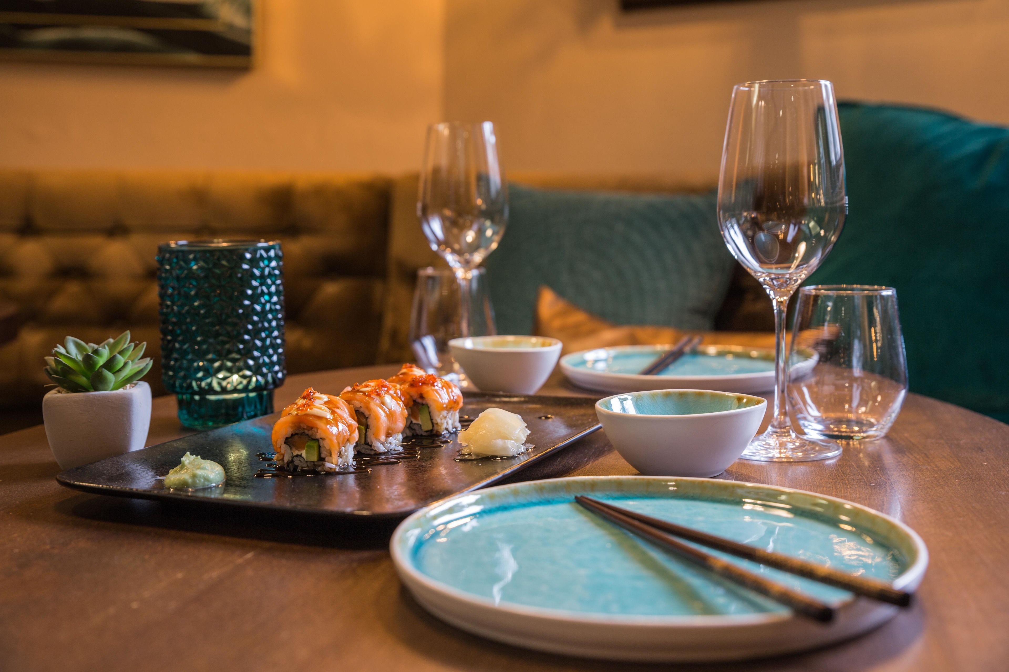 Uma mesa de jantar com sushi, tigelas, hashis e copos de vinho.