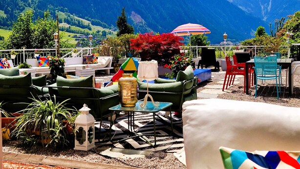 Una terraza con mobiliario exterior, vistas a montañas y una alfombra colorida.