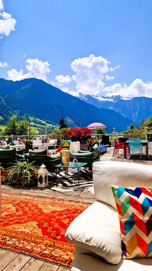 Una terraza con mobiliario exterior, vistas a montañas y una alfombra colorida.