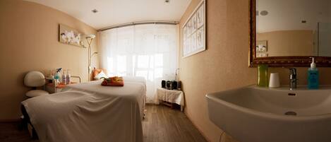 A hotel room with a bed, a large sink, and a window with sheer curtains.