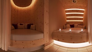 Una habitación circular de madera con una cama y una bañera, ambas con ropa y almohadas blancas. Hay velas sobre la bañera.