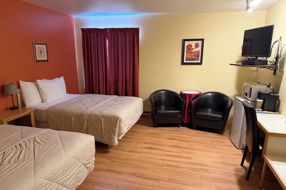 A hotel room with a bed, two chairs, a desk with a computer, a TV, and a microwave.