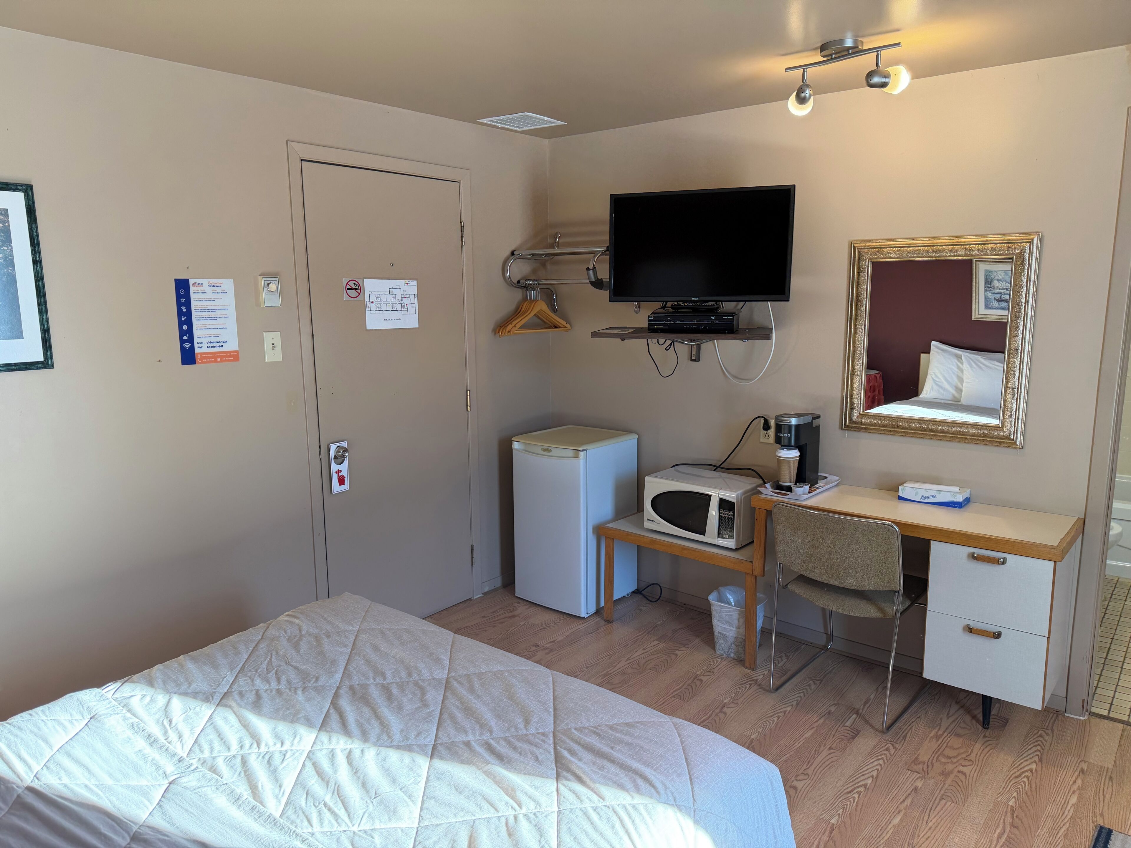 Une chambre d’hôtel équipée d’un lit, d’un bureau avec un micro-ondes, d’une télévision et d’un miroir.