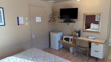Une chambre d’hôtel équipée d’un lit, d’un bureau avec un micro-ondes, d’une télévision et d’un miroir.