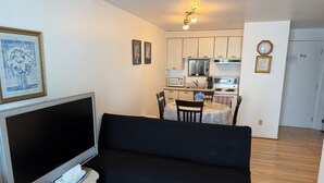 Uma sala de estar com televisão, sofá e um espaço de jantar com cadeiras e mesa.