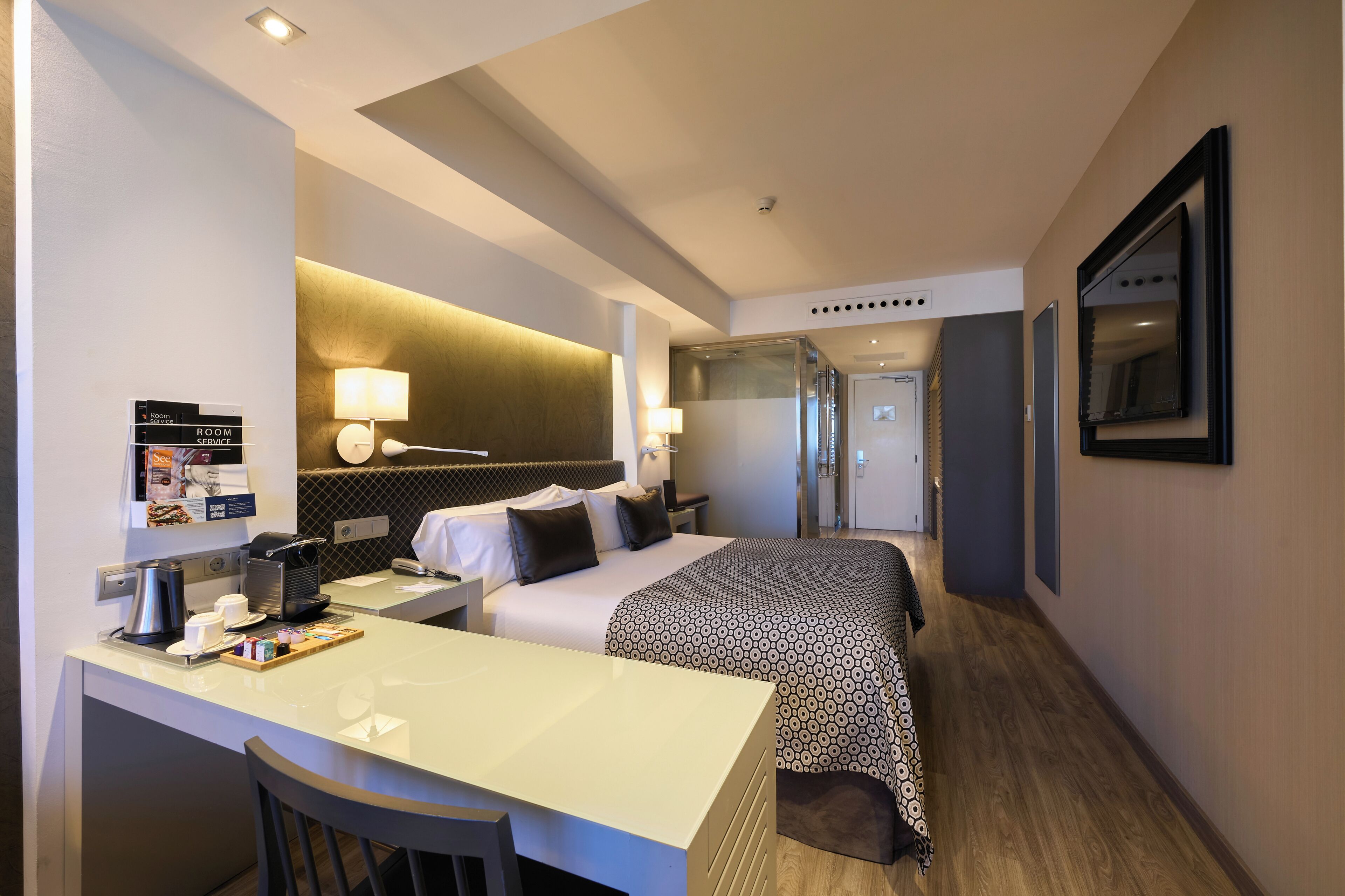 A hotel room with a bed, desk, chair, and a bathroom visible in the background.