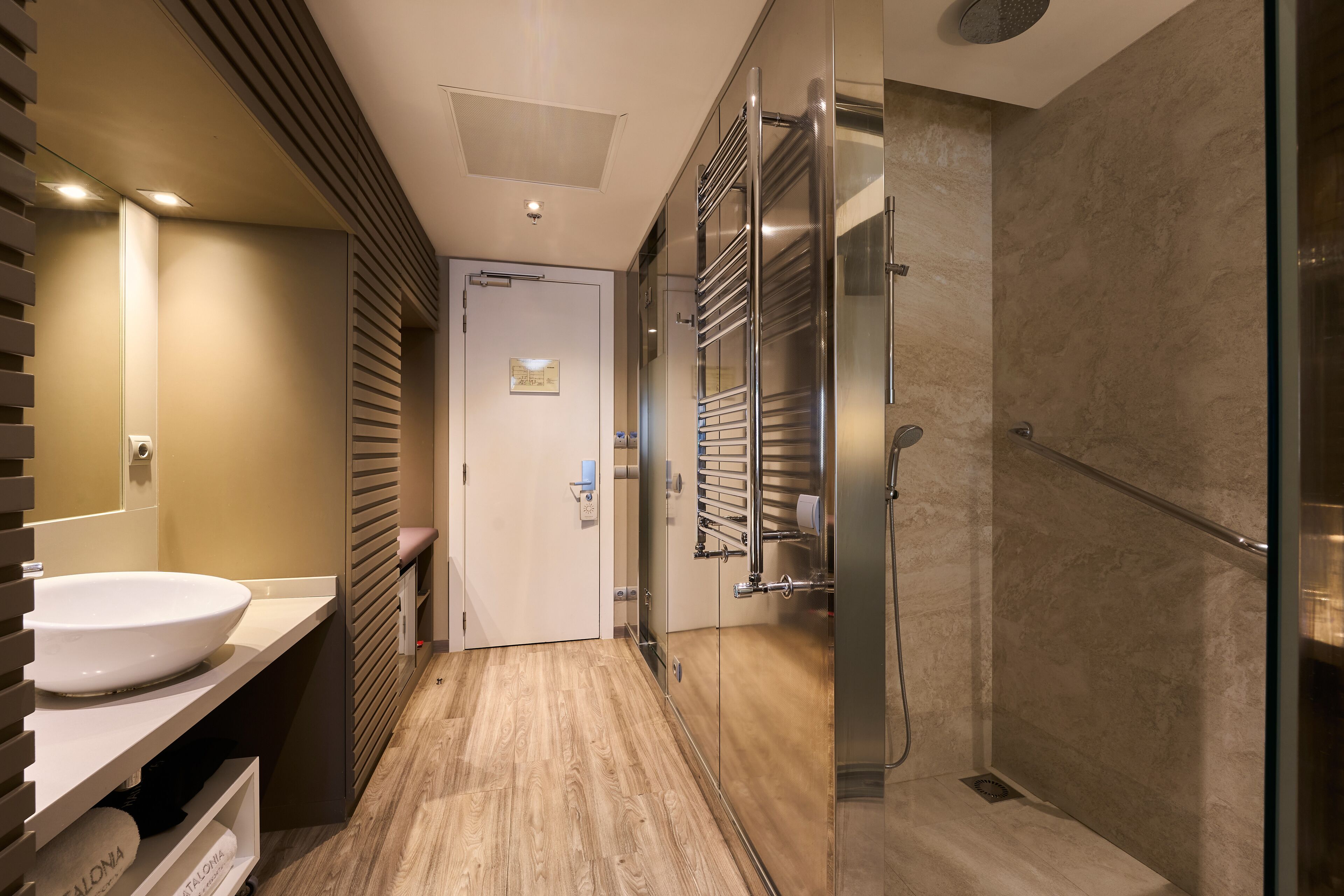 A modern bathroom with a large sink, a glass shower enclosure, and a wooden floor.