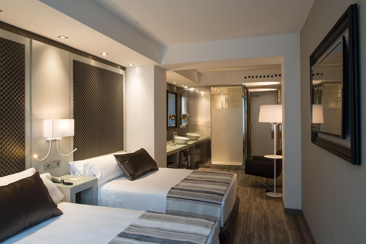 A hotel room with two beds, a bathroom, a mirror, and a small seating area.