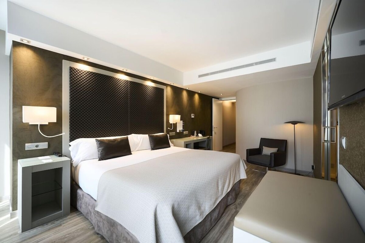 Una habitación de hotel moderna con una cama grande, una mesita de noche, una silla y un armario.