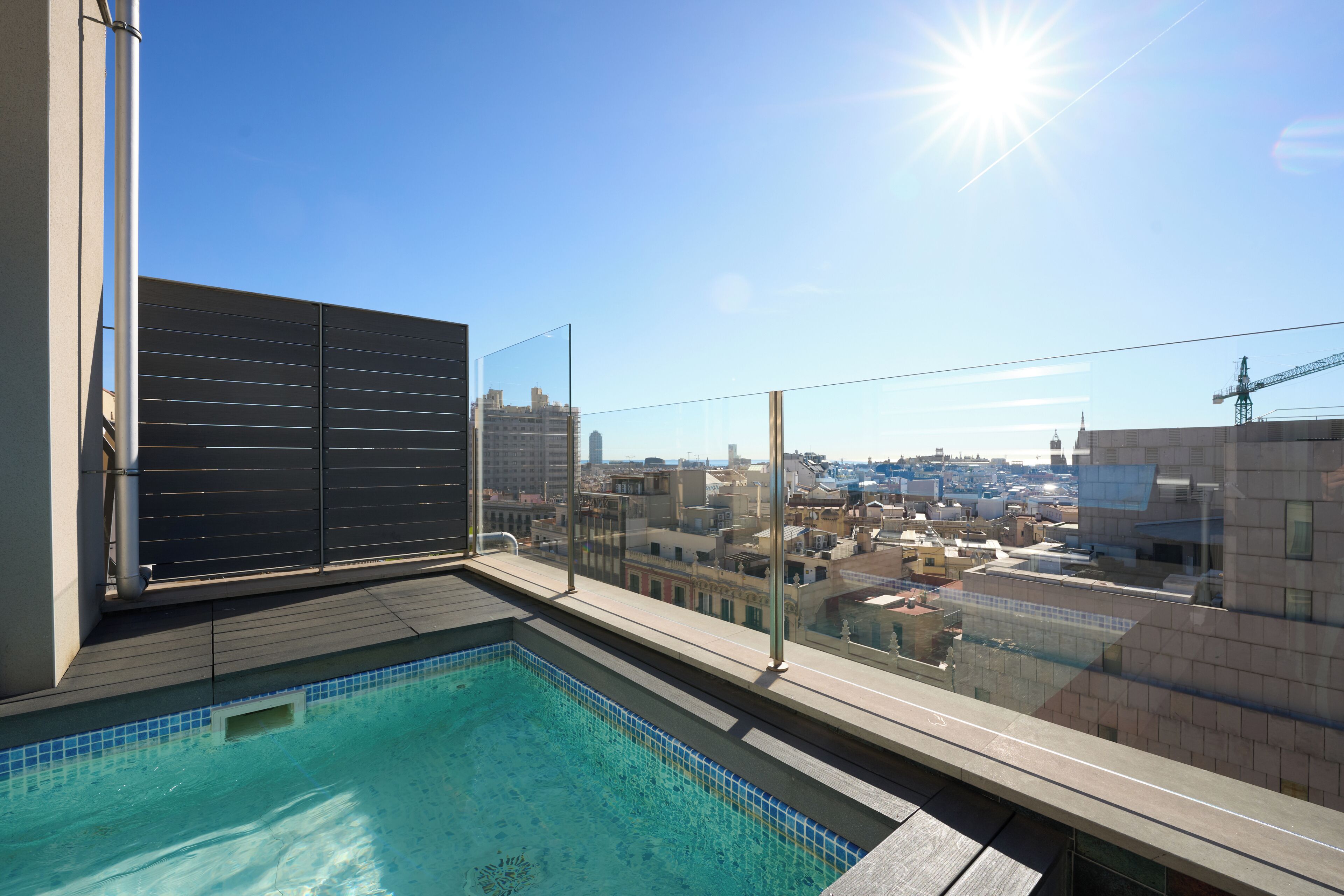 Piscina no terraço com vista para a cidade, guarda-corpo de vidro e céu claro.