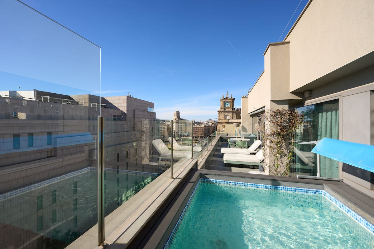 A rooftop pool with clear blue water, surrounded by glass railings and lounge chairs.