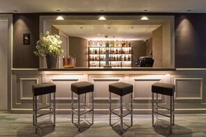 A bar area with a shelf of liquor bottles, three stools, and a potted plant. - Catalonia Square (Barcelona)