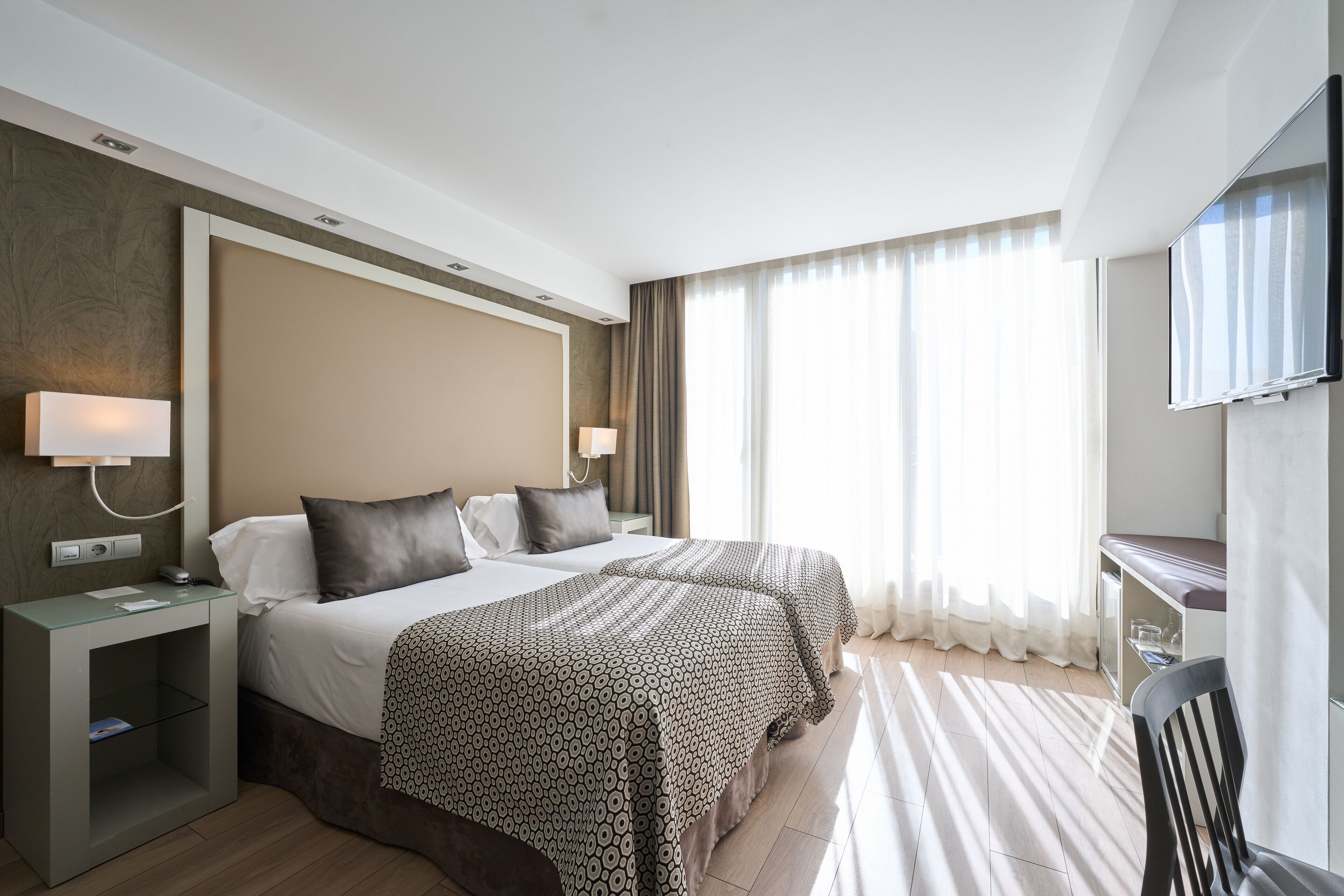 Habitación de hotel con dos camas, un escritorio, una silla y un televisor.