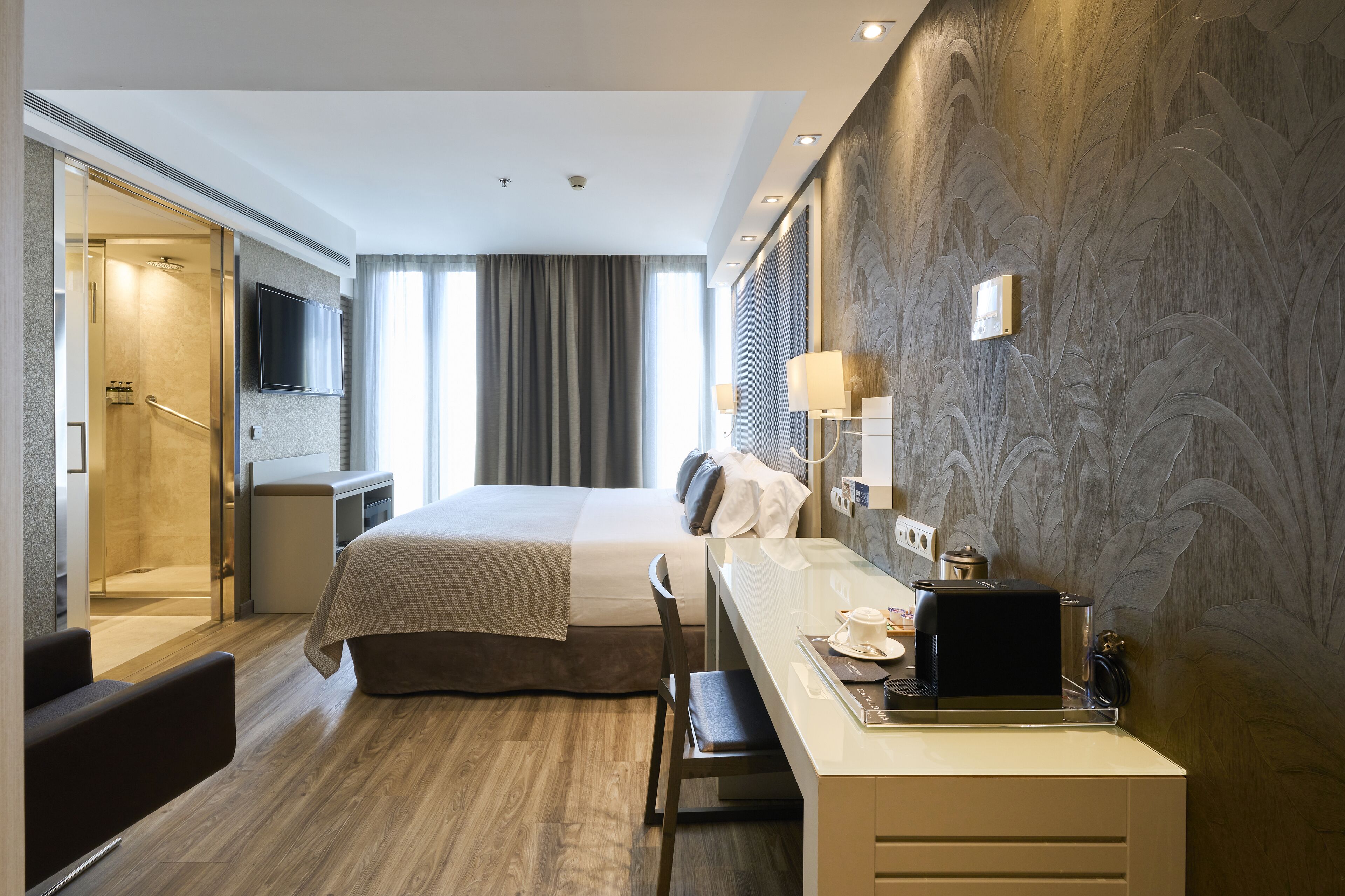 Una habitación de hotel moderna con una cama grande, un escritorio con silla, televisión y zona de ducha.