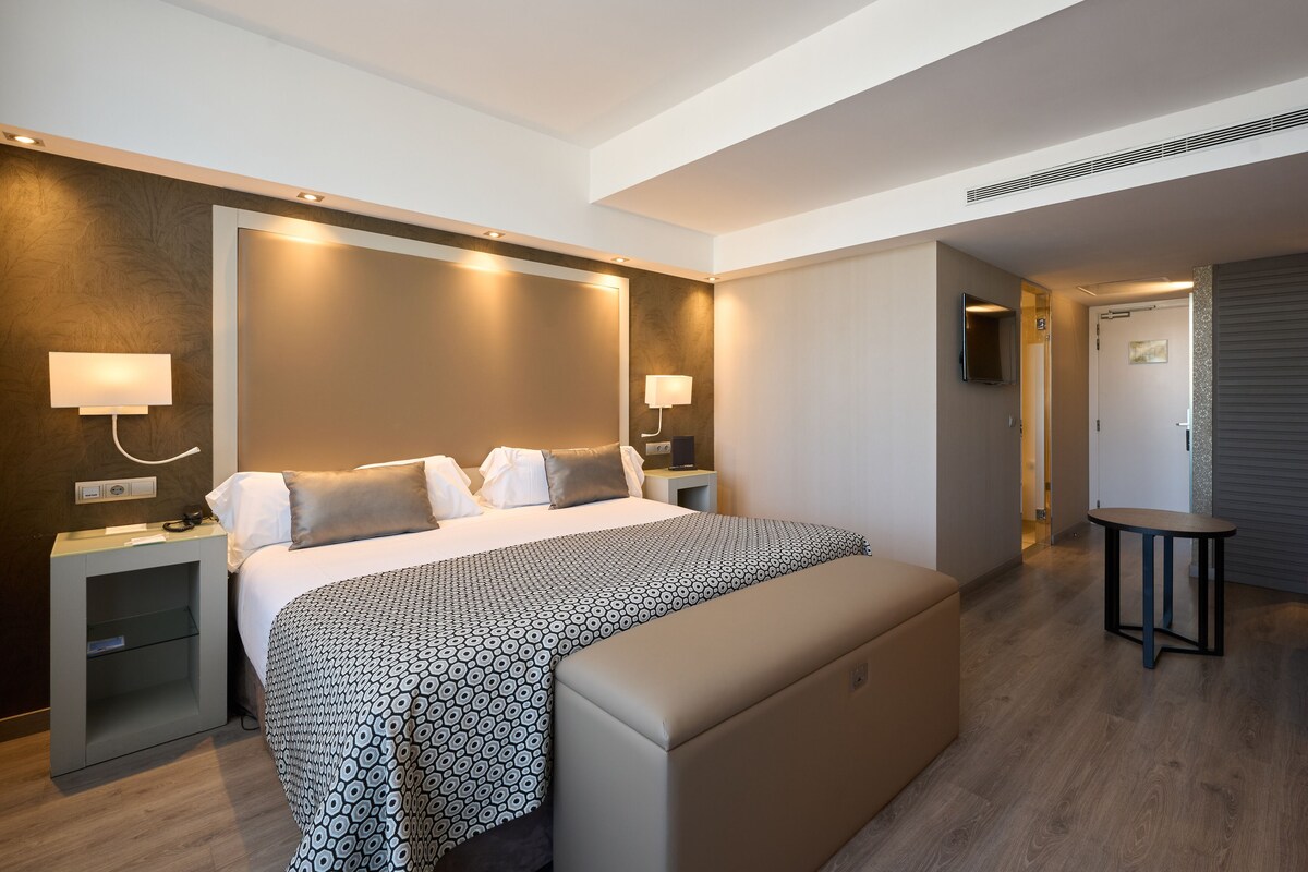 A modern hotel room with a large bed, bedside tables, a bench, and a TV.