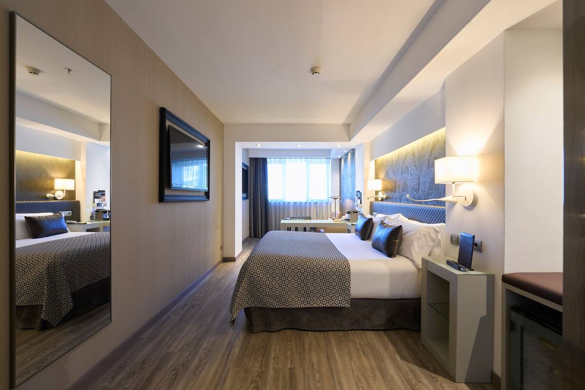 A hotel room with a large bed, bedside tables, a mirror, and a view of the hallway.
