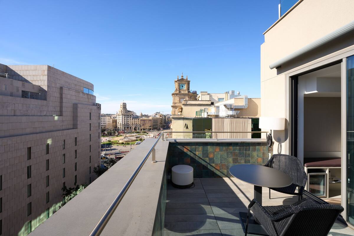 A rooftop terrace with a table and chairs, a view of the cityscape, and a clock tower in the distance.