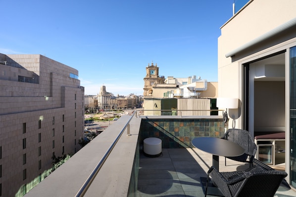 Une terrasse sur le toit, avec une table et des chaises, offrant une vue sur le paysage urbain et, au loin, une tour de l’horloge.