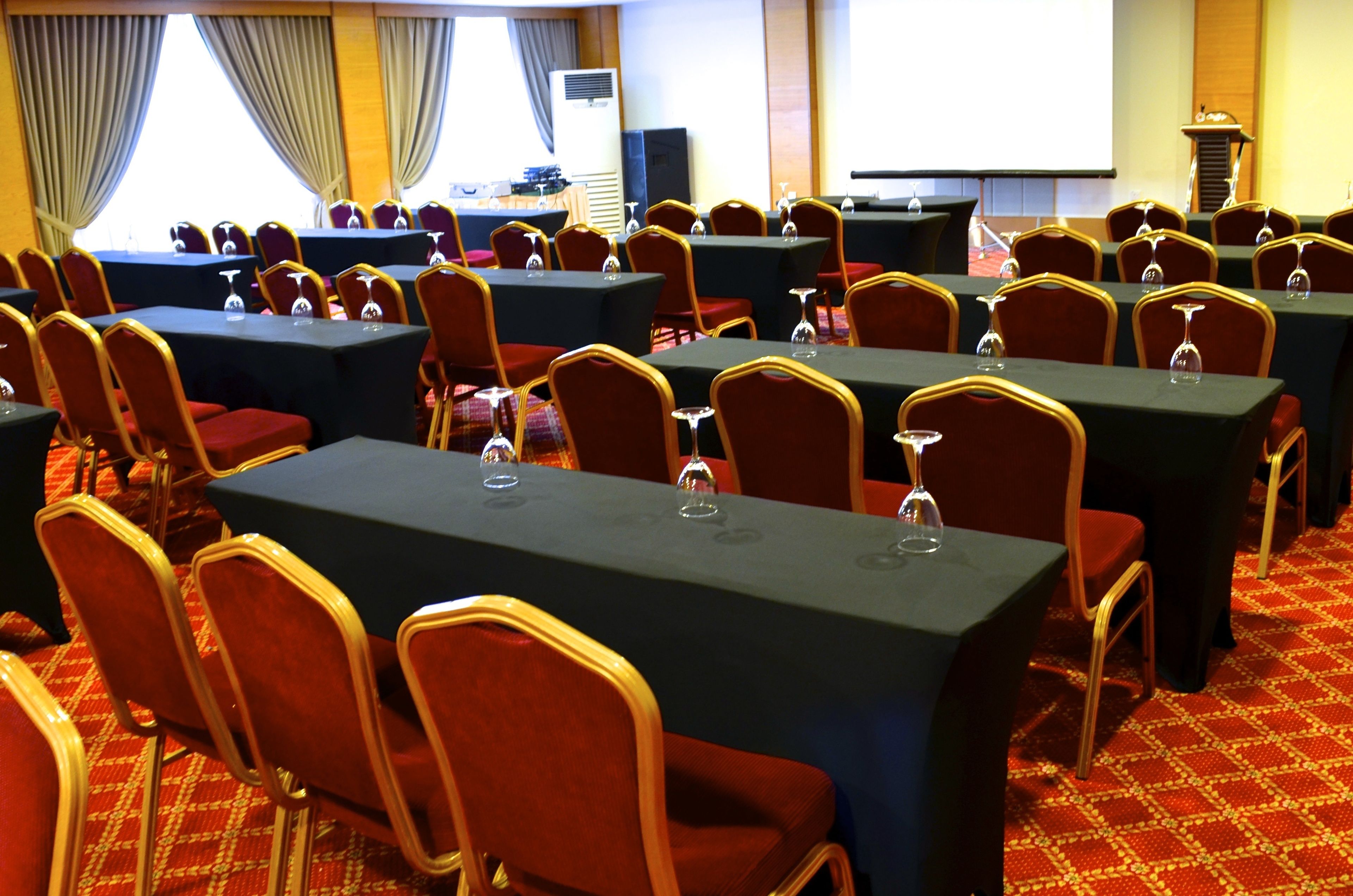 Un salón de conferencias con varias mesas y sillas, equipado con micrófonos y proyectores.