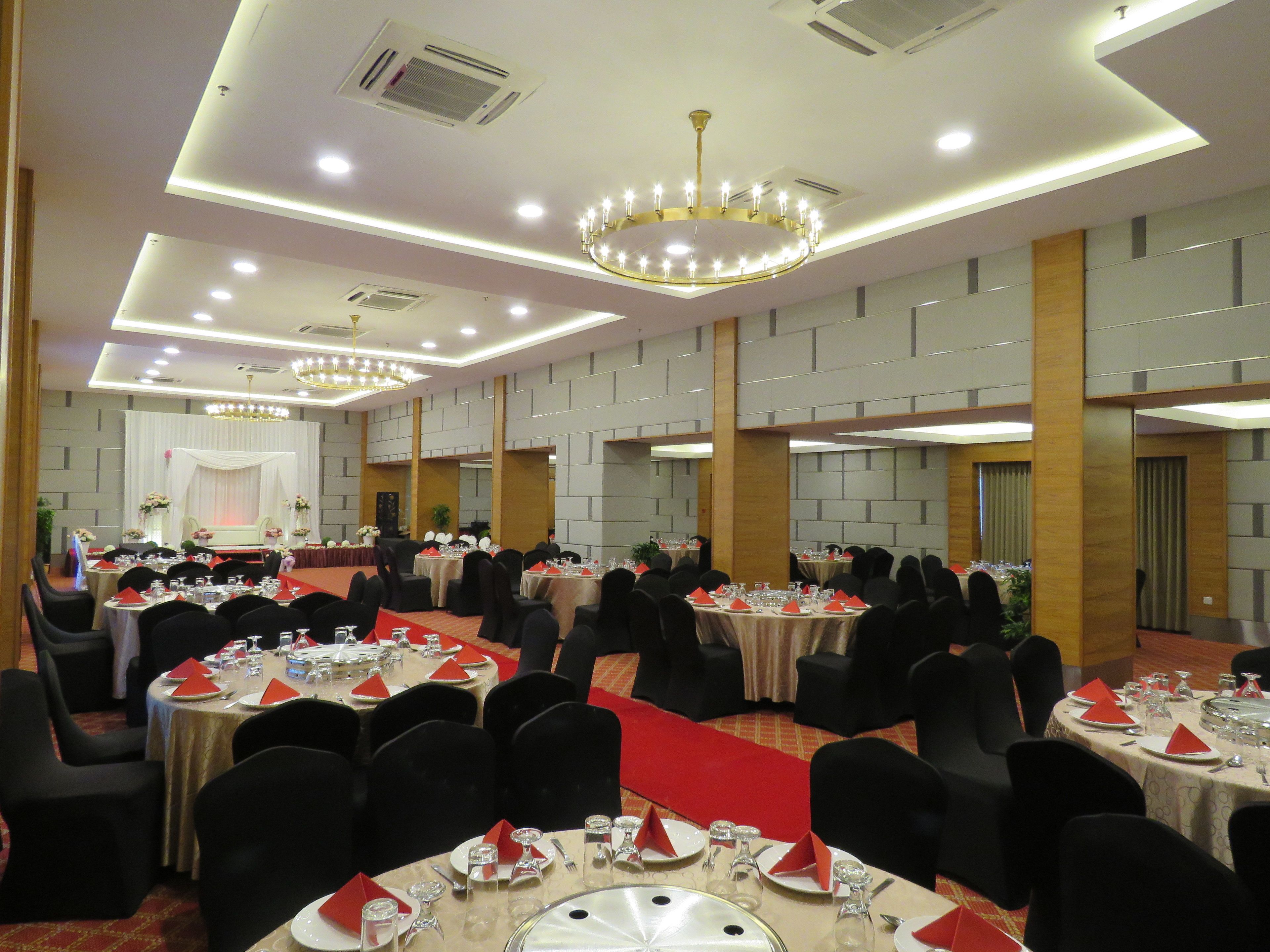 A banquet hall with round tables, black chairs, and red napkins.