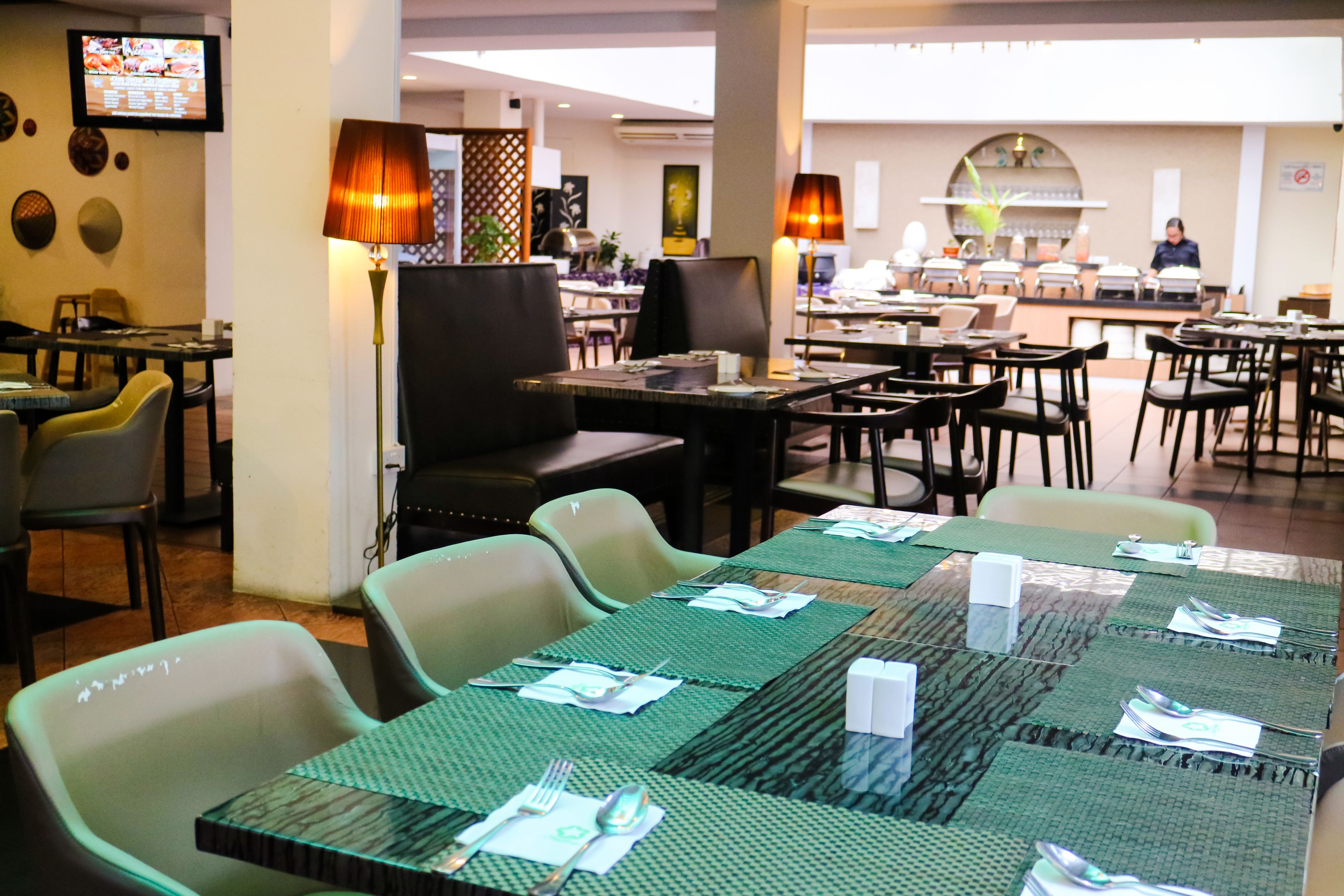 Un restaurante con varias mesas dispuestas para comer, con manteles individuales verdes y cubiertos.