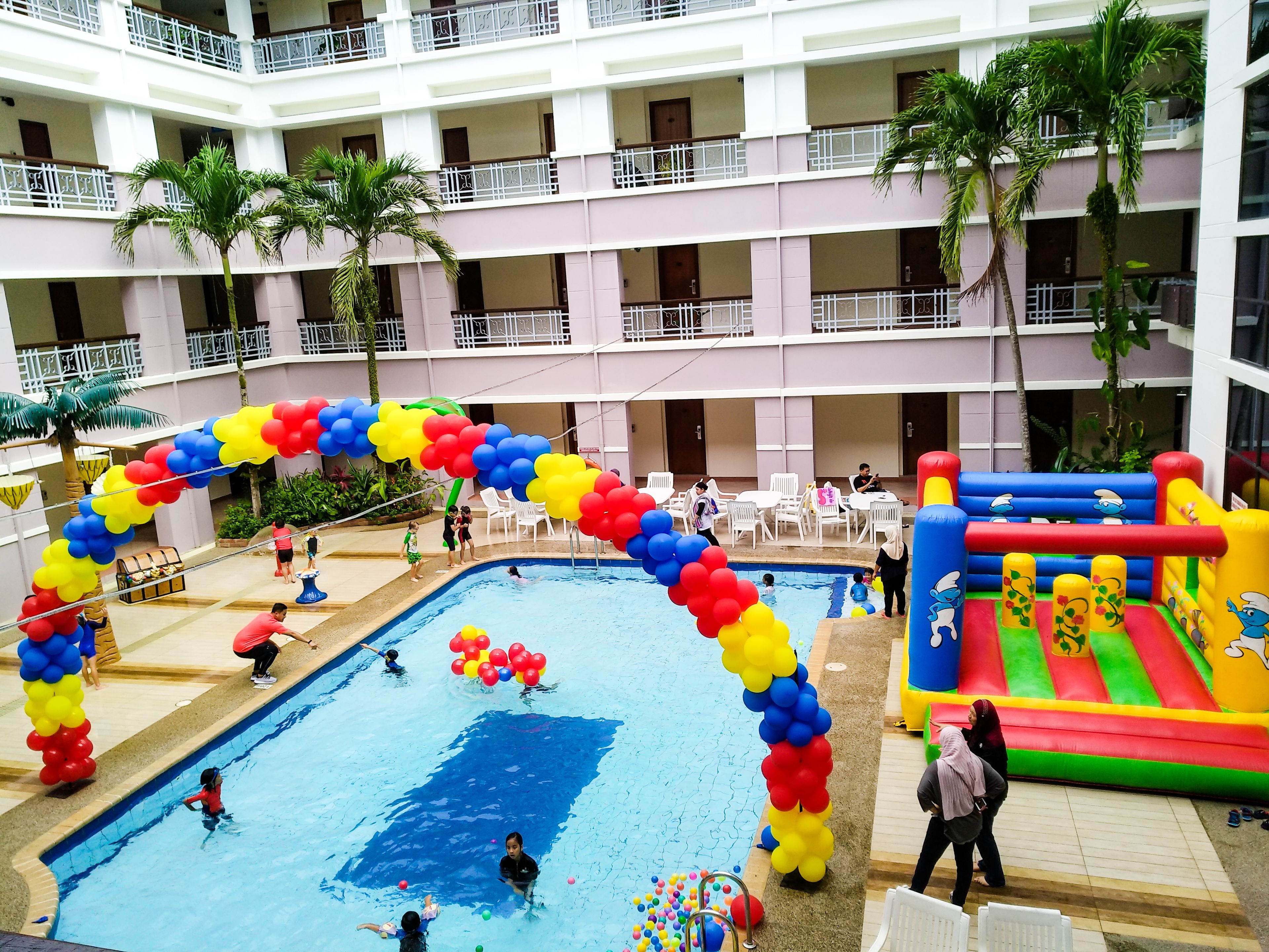 Un hotel de varios niveles con piscina, zona de juegos inflable y mobiliario exterior.