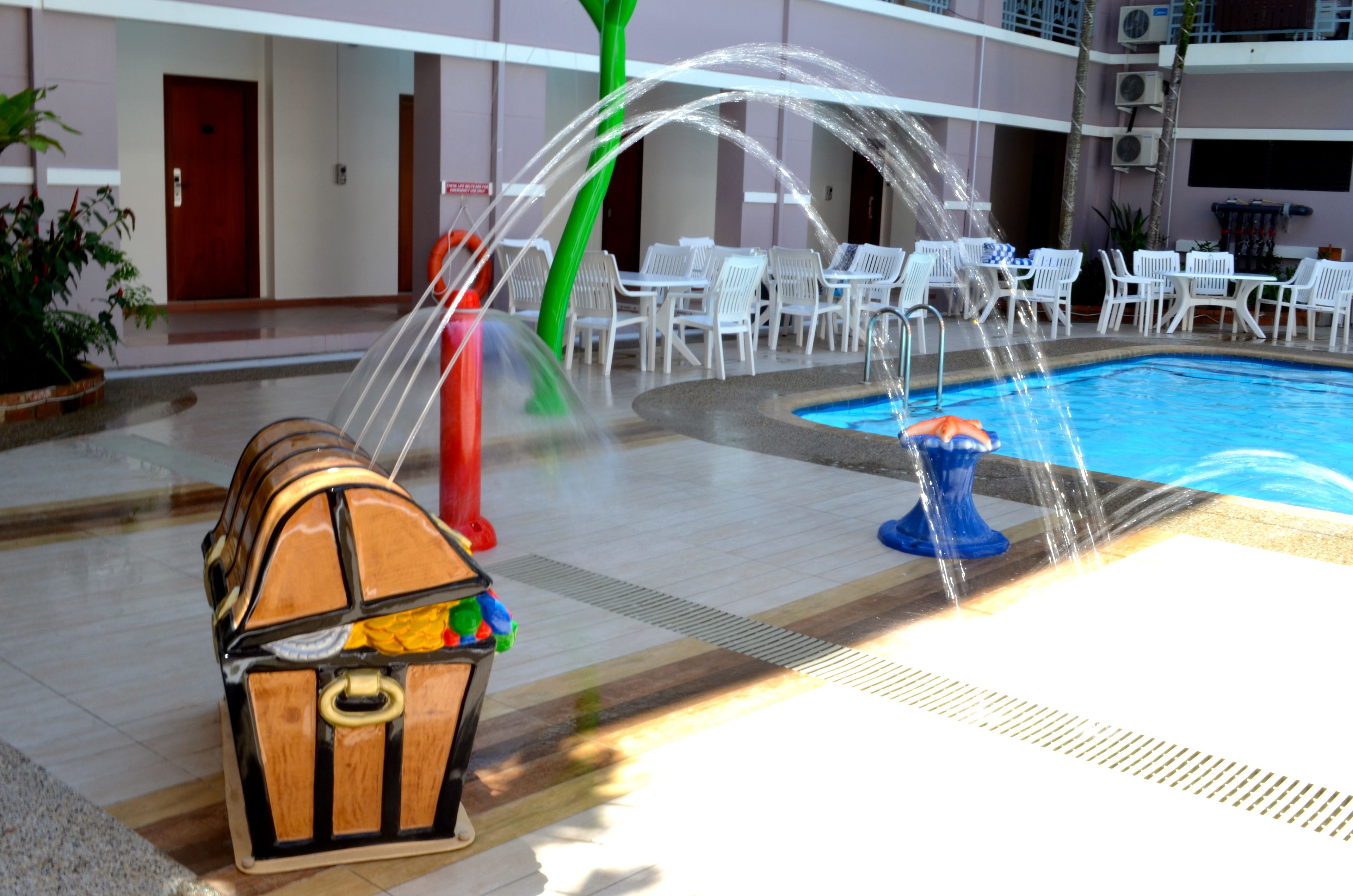 A pool area with a water feature, lounge chairs, and a wooden chest.