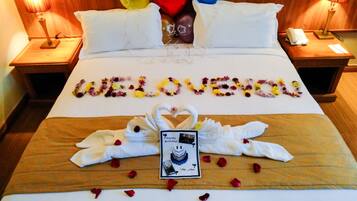 Habitación de hotel con una cama decorada con la palabra 'LOVE' hecha de flores, un arreglo de toallas con forma de cisne y una tarjeta de cumpleaños.