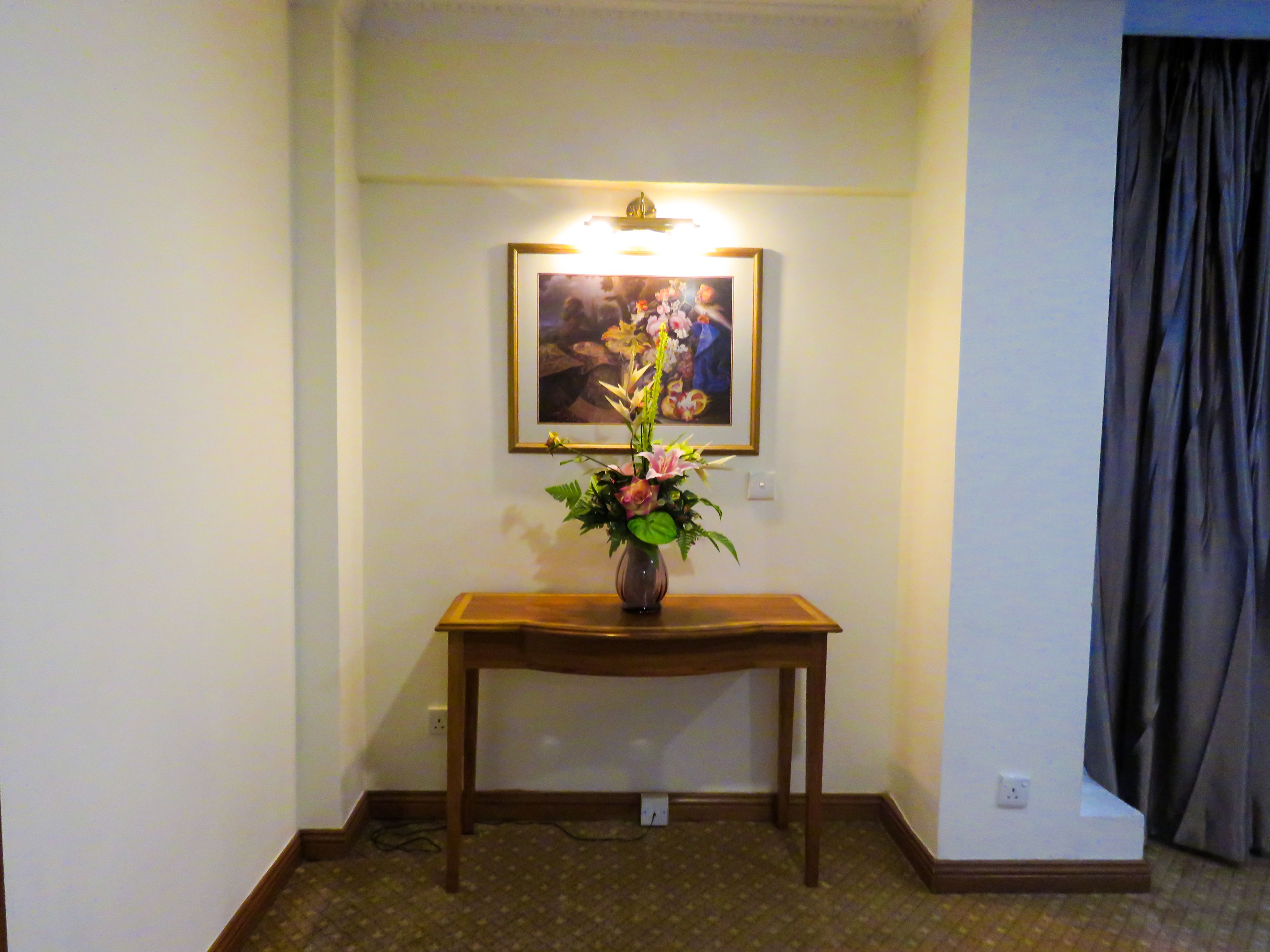Una habitación con una consola de madera, un jarrón con flores y un cuadro en la pared.