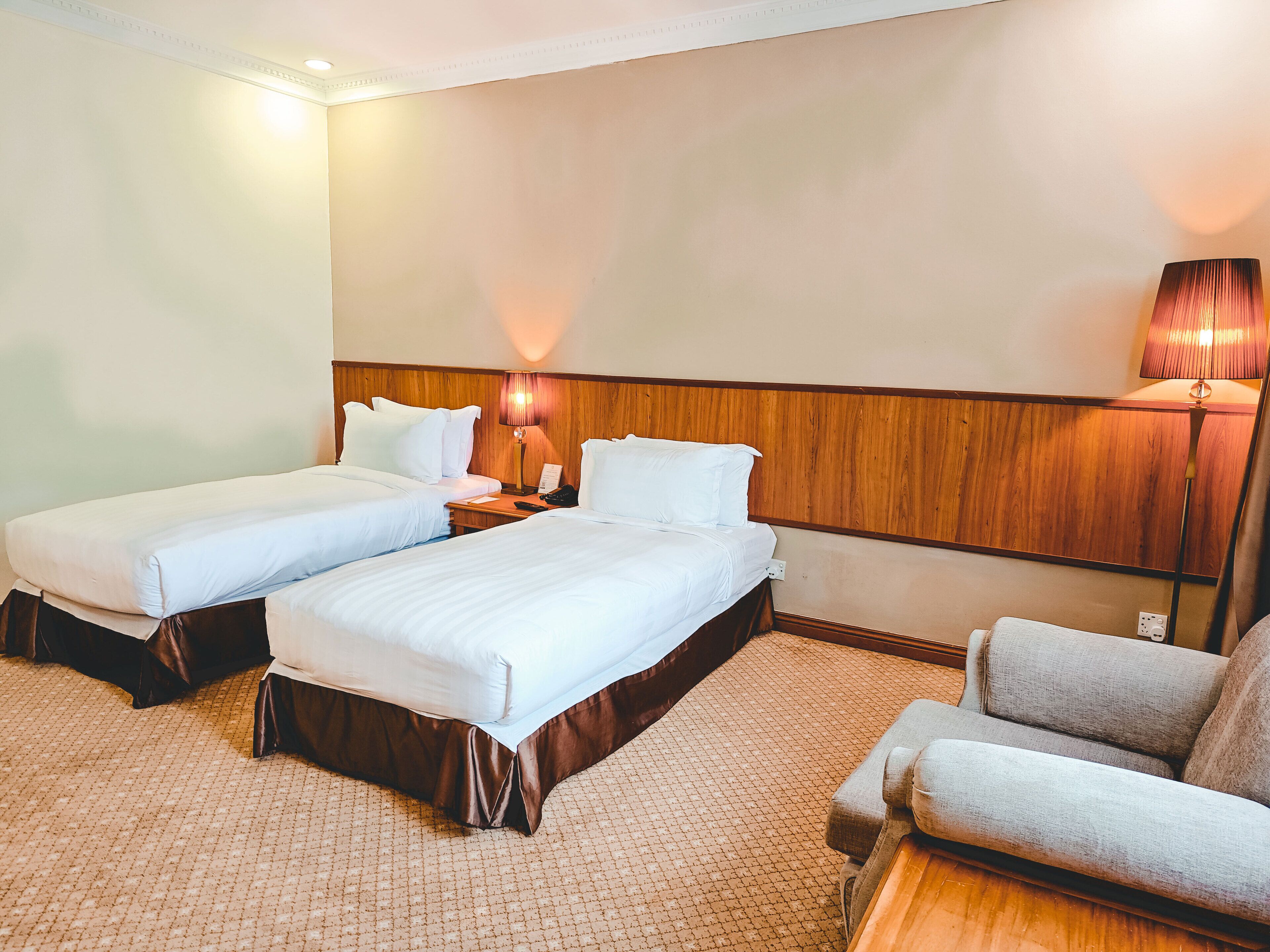 A hotel room with two beds, a nightstand, a lamp, and a sofa.