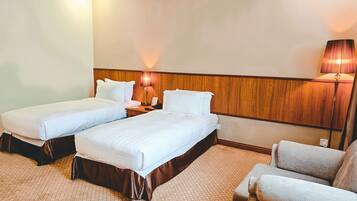 A hotel room with two beds, a nightstand, a lamp, and a sofa.