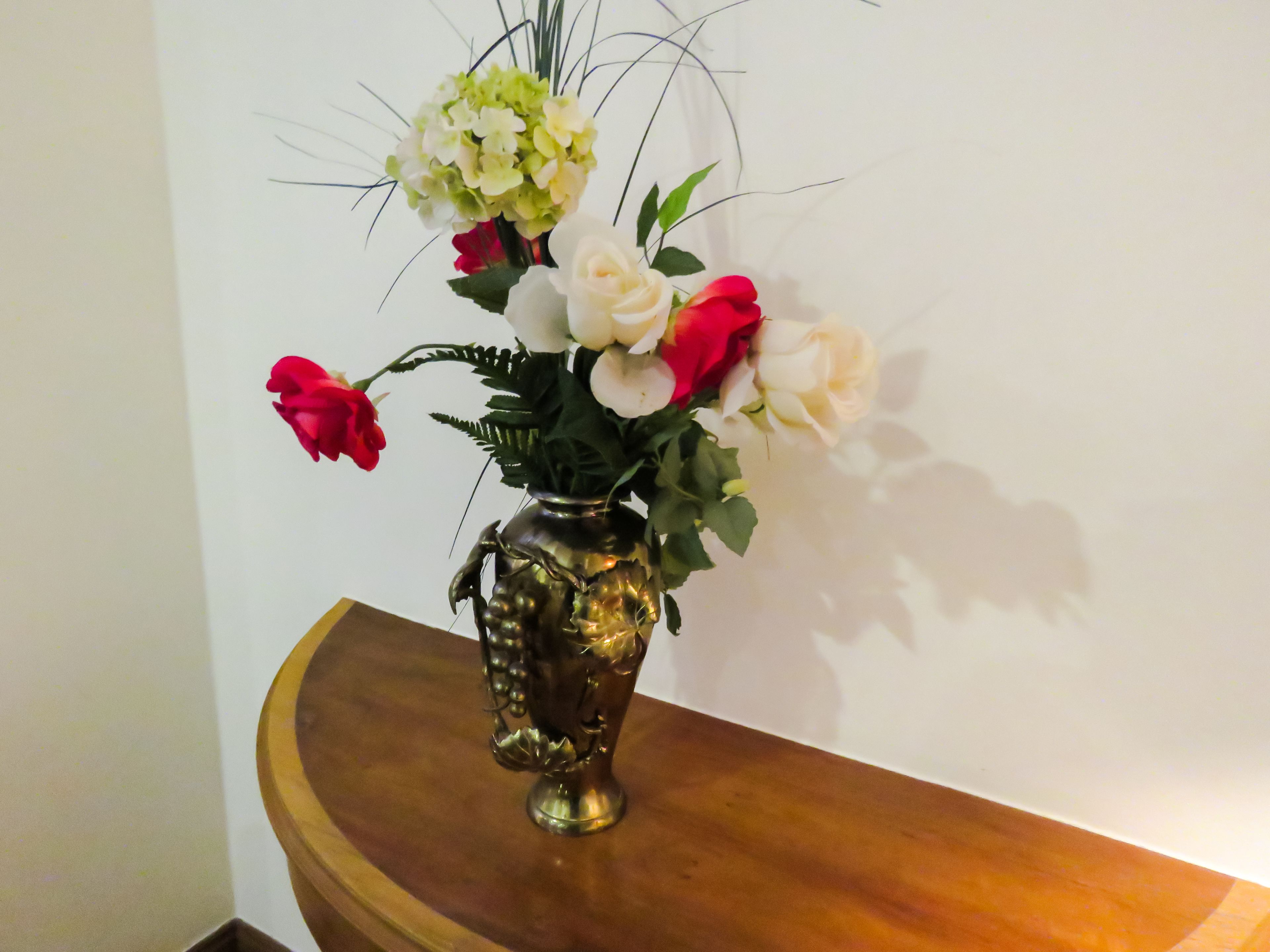 Un vase rempli de fleurs est posé sur une table en bois, devant un mur blanc.