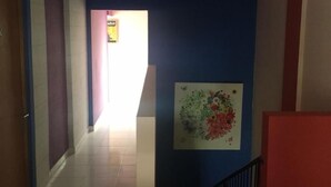 Un pasillo con pared azul, pilar blanco y barandilla roja.
