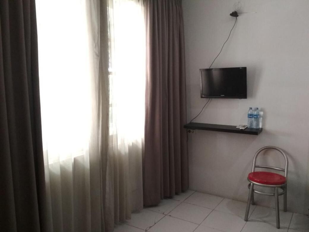 Una habitación con un televisor montado en la pared, una silla con asiento rojo y un estante con botellas de agua.