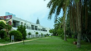 A modern building with a white facade, surrounded by a well-maintained grassy area and palm trees. - Kkaras Hotel (Ayia Napa)