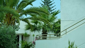 A white building with a staircase and lush greenery including palm trees and other plants. - Kkaras Hotel (Ayia Napa)