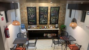 Una cafetería con mesas y sillas, un dispensador de agua y pizarras con mensajes sobre café.