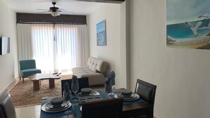 Un comedor con una mesa dispuesta para cuatro, un ventilador de techo, un sofá y un cuadro de una gaviota.