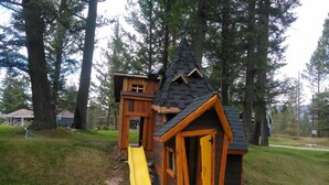 A wooden playhouse with a yellow slide and a small porch. - Fairmont Mountain Bungalows (Fairmont Hot Springs)