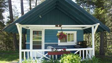Une cabane avec une véranda, une table à manger et un barbecue.