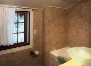 Une salle de bain avec des carreaux de couleur beige, une fenêtre avec un rideau, un porte-rouleau de papier toilette et un lavabo en verre.