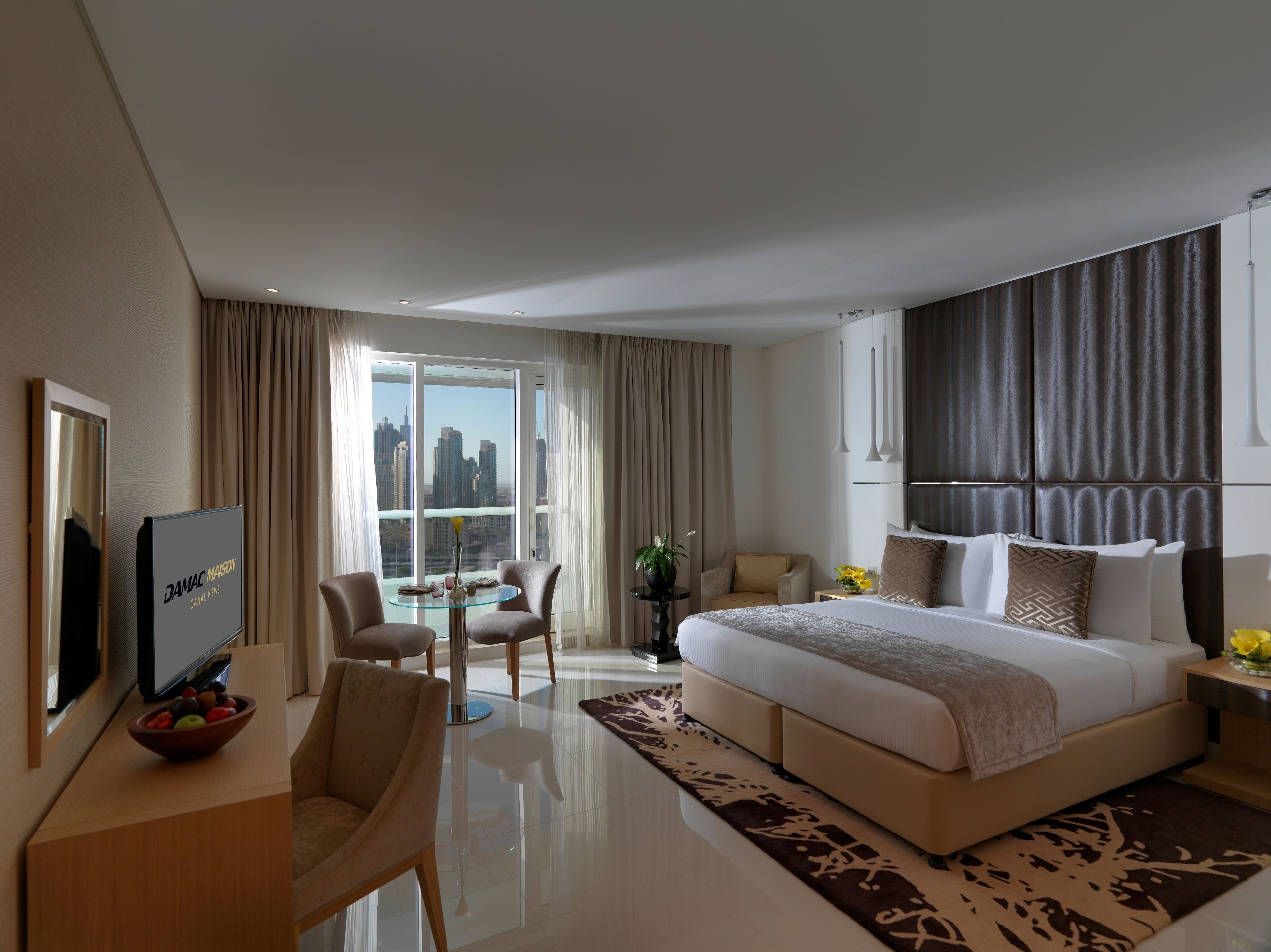 Ein modernes Hotelzimmer mit einem großen Bett, einem Schreibtisch mit Fernseher, einem Essbereich und Blick auf die Stadtlandschaft.