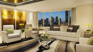 Un salon moderne avec vue sur la ville, comprenant un canapé, des fauteuils et une table basse en verre.