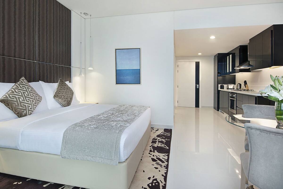 Une chambre d’hôtel moderne, équipée d’un lit, d’une table de chevet et offrant une vue sur la cuisine.