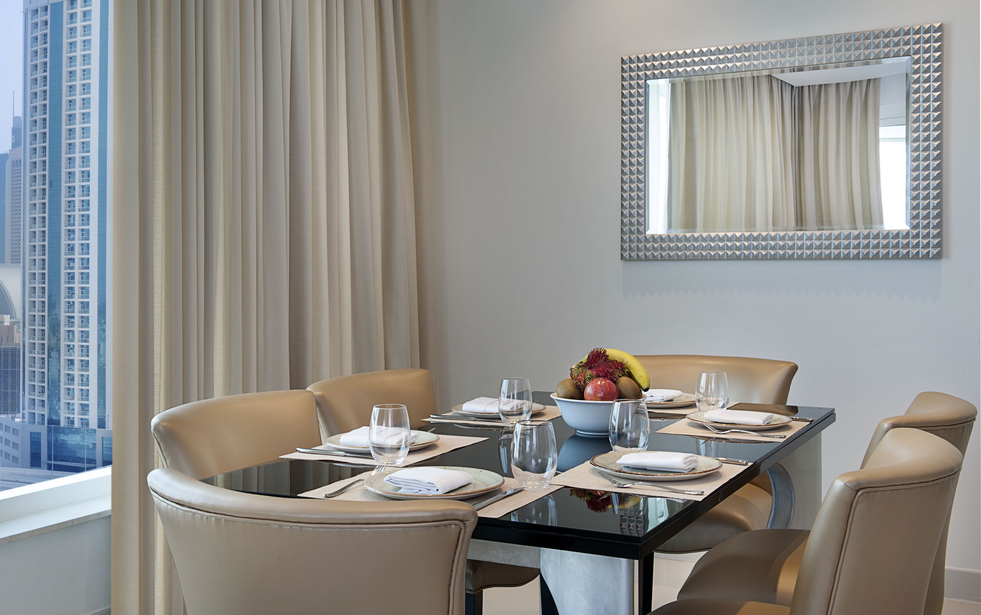 A dining area with a glass table, beige chairs, and a fruit bowl.